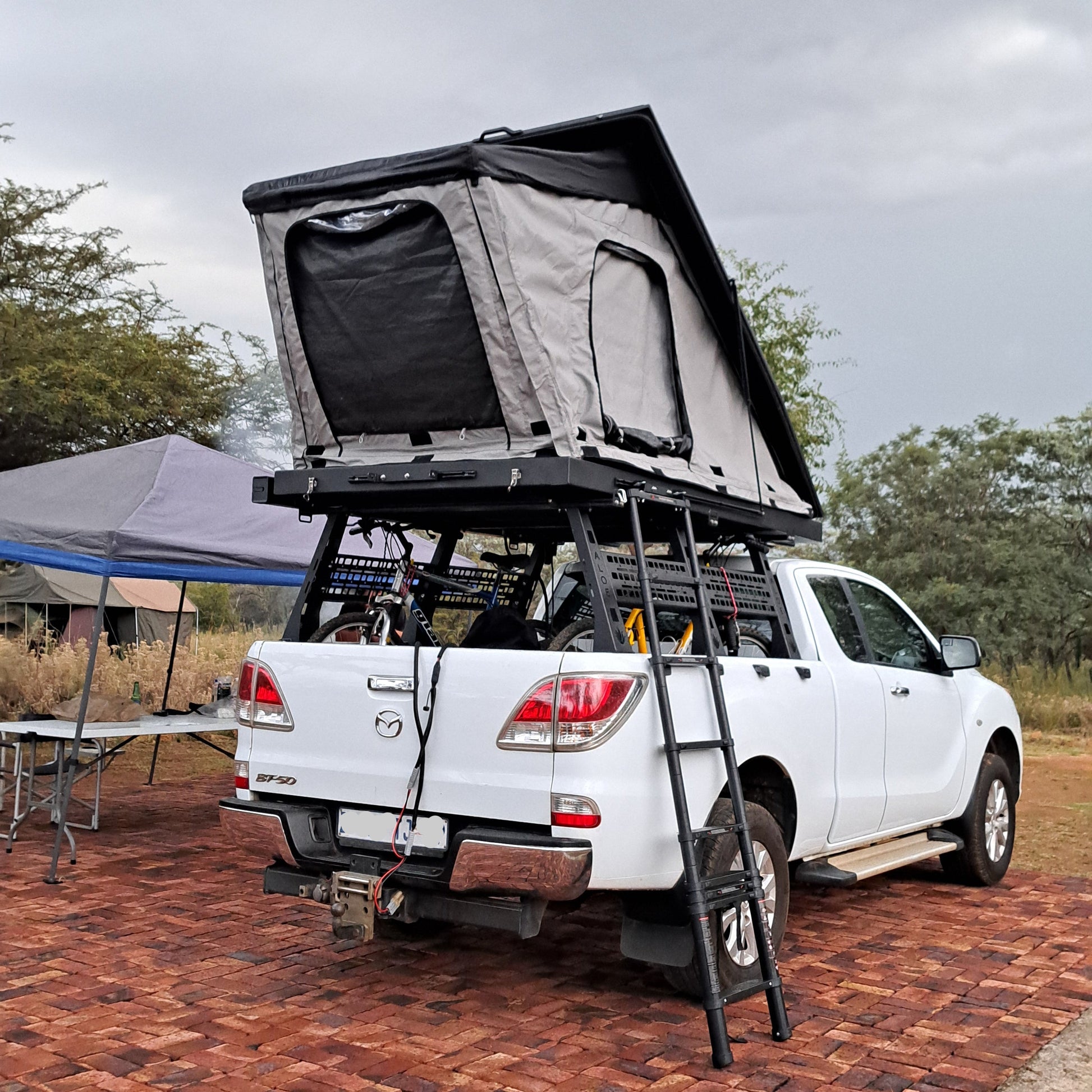Black and grey roof top tent with a ladder on top of a Mazda 4x4